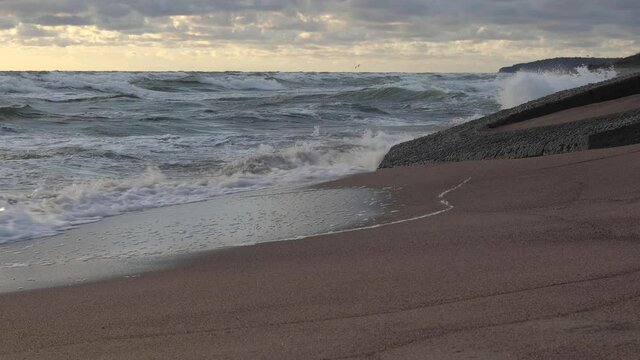 Windy weather on Klaipeda beach in Lithuania at sunset. Waves crashes on concreate ruins of WW II defence fortifications.