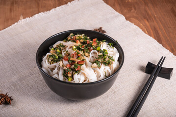 Rice noodles with herbs, vegetables and soy sauce in a bowl with chopsticks on a linen napkin, close-up, top view