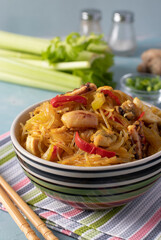 Rice noodles Funchoza with seafood. Cellophane pasta, mussels, squid and octopus, healthy Asian meal snack in a bowl on a light blue background. Close-up