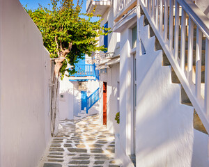 Traditional narrow cobbled streets, beautiful alleyways of Greek island town. Whitewashed houses, olive trees, blue balconies, stairs. Mykonos, Greece