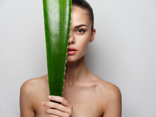 nude woman with green aloe leaf on light background cropped view model
