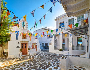Beautiful morning view of small square decorated for some celebrations with flags in typical Greek town. Greek Orthodox church, whitewashed houses.