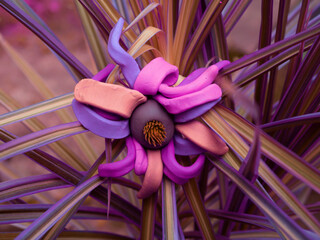 Purple mixed color clay art flower affixed on long leaves plant at natural park background.