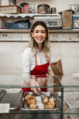 Beautiful young female seller working in a confectionery shop or bakery. She is selling and packing delicious sweets.