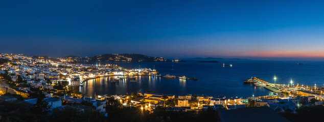 Obraz premium Beautiful night panorama of Mykonos, Greece, ships, port, whitewashed houses. Town lights up. Vacations, leisure, nightlife, Mediterranean lifestyle