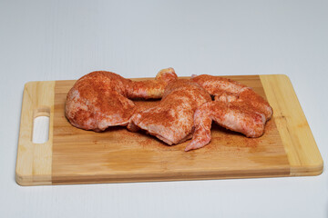 Chicken thighs and wings are sprinkled with barbecue spices. The meat is on a wooden board.