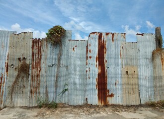 Zinc wall, gray, yellow rust, blue sky with white clouds.
