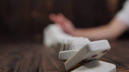 Close-up of a domino falling on a table, blurred background. The domino effect.