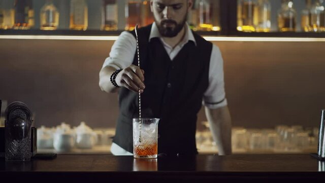 The bartender prepares a cocktail at the bar. A man mixes ice with alcohol in a restaurant preparing a cocktail.