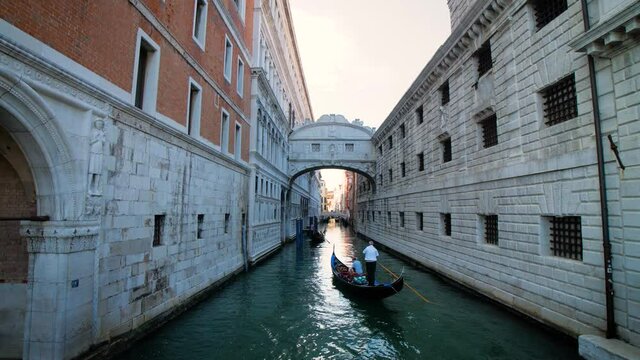 The famous Bridge of Sighs (Ponte dei Sospiri) in Venice, Italy during the day. Venice, Veneto, Italy - 06/06/2021: A gondolier with tourists pass under the bridge next to Piazza San Marco. 4K.