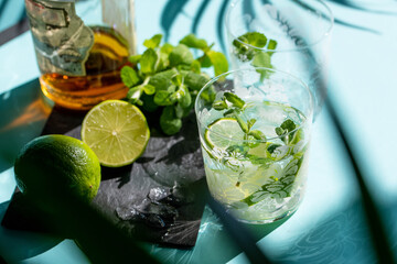 Summer cocktail Mojito preparation: lime slices, peppermint and ice on a black board.