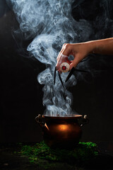The witch's hand put her eye in the smoking cauldron.
