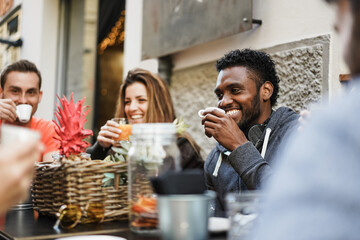 Happy multiracial friends eating and drinking outdoor at vintage bar restaurant - Main focus on african man face