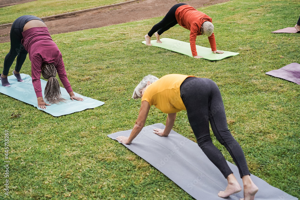 Wall mural Senior people doing yoga class at city park - Focus on african woman