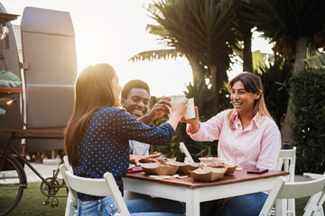 Multiracial people eating and cheering at food truck restaurant outdoor - Focus on african man face