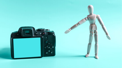 The figure of a wooden man pointing at the camera screen with his hand. The figure of a wooden man and an empty blue screen