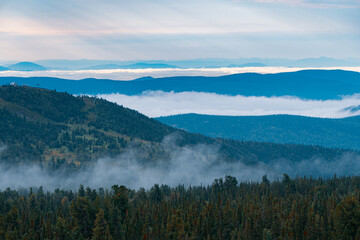 Naklejka premium Panorama of a summer mountain valley with peaks of the mountain range, clouds and fog. Forest in the foreground. View from the top.