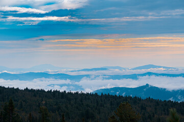 Obraz premium Panorama of a summer mountain valley with peaks of the mountain range, clouds and fog. Forest in the foreground. View from the top.