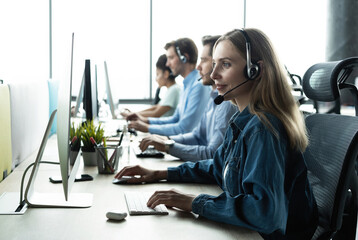 How can I help you? Beautiful call center workers in headphones are working at modern office