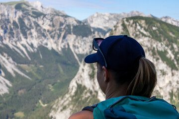 A woman with a hiking backpack admiring the view on the Alpine mountain chains in Austria, Hochschwab region. The slopes are partially overgrown with small bushes, higher parts baren. Happiness