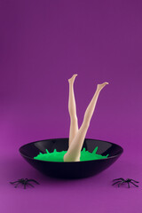 Witch's neon green soup with legs and black spiders on purple background. Minimal Halloween concept.