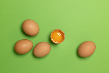 Easter brown chicken eggs and one broken egg with yolk on green background