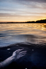 A mysterious scary hand of drowned woman or mermaid underwater at sunset