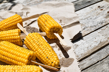 Roasted sweet corn cobs are on the recycled paper on the wooden table in the summer garden