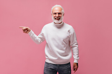 Cheerful man in jeans and sweater smiling and pointing to place for text. Modern grey haired guy...