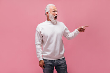 Shocked man in white sweater pointing to place for text. Surprised adult guy in eyeglasses and...