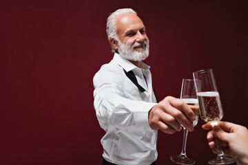 Happy man in white shirt clinking champagne glasses. Joyful guy with grey beard posing with vine on isolated background..