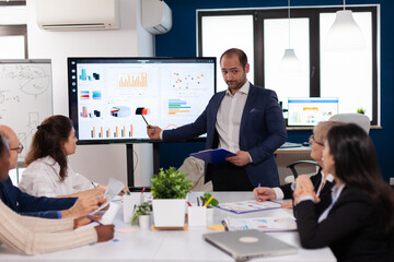 Successful team leader briefing pointing explaining project in conference room brainstorming. Corporate staff discussing new business application with colleagues looking at screen