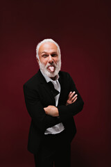 Cheerful man demonstrates tongue on burgundy background. Funny guy with beard in black suit and...