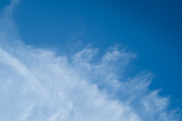 Whispy white clouds and blue sky diving frame diagonally with negative space for copy