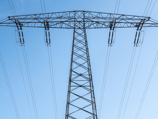 Teilausschnitt von einem Strommast mit sechs Leitungen unter blauem Himmel