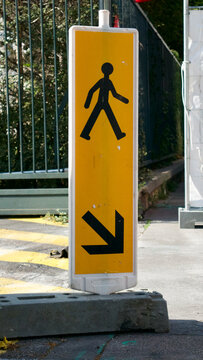 Yellow and black road sign by a construction site directing pedestrians with an arrow 