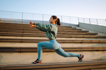 Young fitness woman exercising and stretching outdoors in the morning. Fit healthy athlete is doing workout on the street. Sport, Active life.