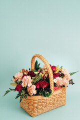 Fototapeta na wymiar A widling bouquet of summer flowers in a wicker basket stands on a delicate blue background. Vertical greeting card with copy space at the top.