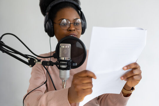 African American woman with headphones and a microphone recording a podcast in a recording studio, Millennial black woman creating audio content, confident woman working in radio or interviewing