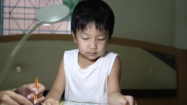 Asian cute child boy having conversation with father while studying and doing homework together  in room with lighting lamp background. Concept of children education, school at home.