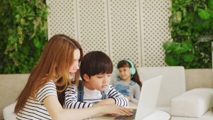 Asian boy and girl sit at desk study online on laptop, smart little kids handwrite in notebook learning using internet lessons on quarantine, homeschooling concept.
