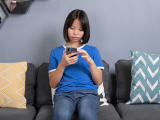 asian girl sit on couch in living room holding smart phone, chatting use social media network, watch received video from friend, with modern wireless technology.