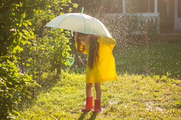 A happy girl with a green umbrella under the summer rain. The girl is dressed in a yellow raincoat...