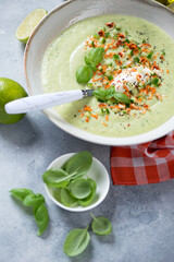 Close-up of cucumber and green basil gazpacho soup topped with cheese, vertical shot on a light-blue stone surface, selective focus