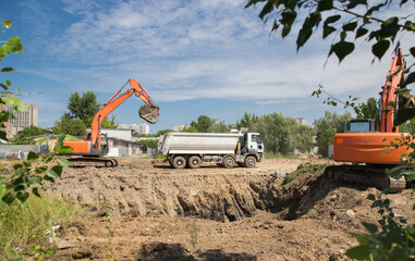 two orange tracked excavators and a gray dump truck in the process of excavation. Site preparation...
