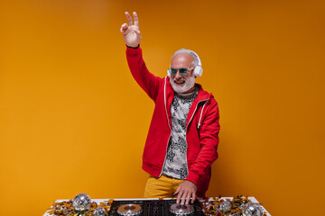 Optimistic man in blue sunglasses shows peace sign and works as dj. Cool adult with good mood with...