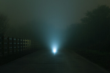 A mysterious spooky glowing light on a road, with a shallow depth of field. On a moody, foggy,...