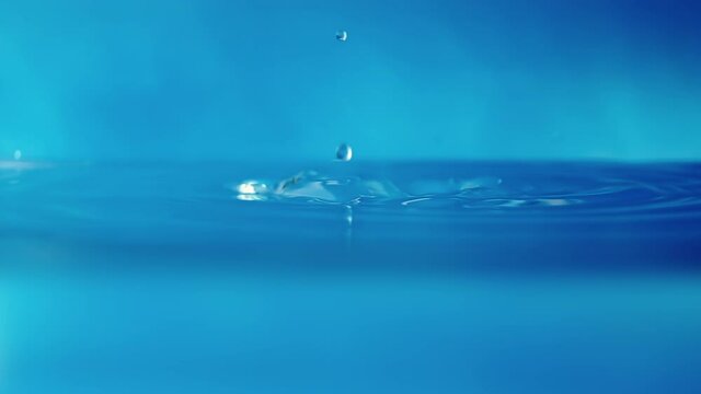 Slow motion video of a water surface with falling drops on a blue background. Splashing water.