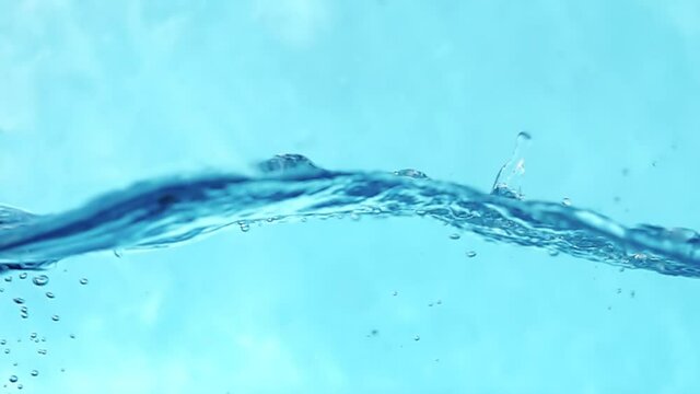 Slow motion video of water waves with splashes and falling drops on a blue background.