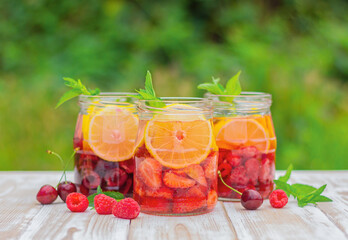 drink from lemon, berries and mint in glass jars on a table in the garden. summer refreshing lemonade.